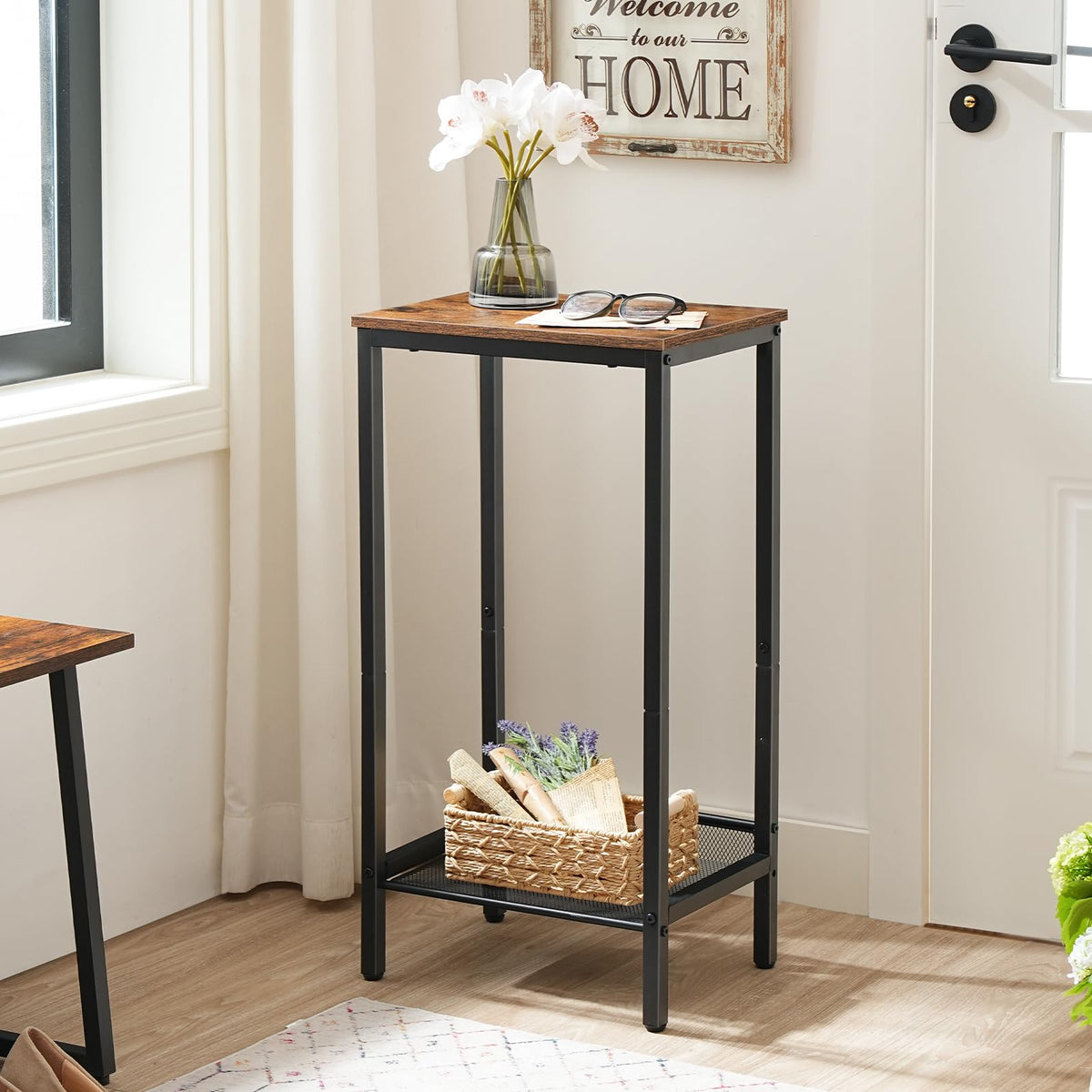 Small wooden table with black metal legs in a room with a 'Welcome to our Home' sign.